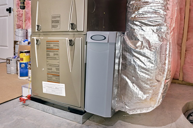 Air handler between high efficiency furnace and ductwork in a basement utility room.