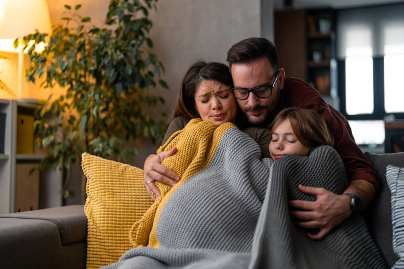 Family of three bundled up on their couch.