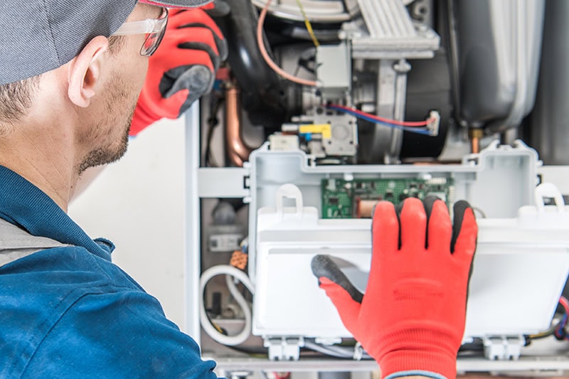 Schedule Your Annual Furnace Inspection Now. A technician inspecting a furnace and making sure it's working properly.